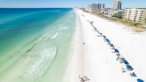 A beach with clear turquoise waters, a long stretch of white sand, and a row of beach umbrellas.
