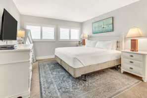 A bedroom with a bed, bedside tables, a TV, and a window with blinds. - Beach House 604C - Gulf Front Resort! (Miramar Beach)
