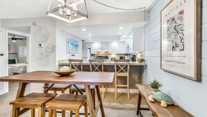 A modern kitchen with white cabinets, a wooden dining table, and a hanging light fixture.