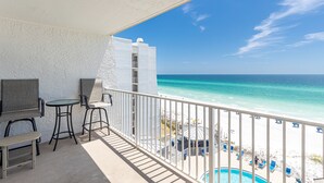 A balcony with a pool, chairs, and a view of the beach and ocean.