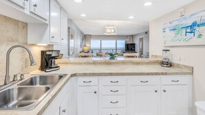 A modern kitchen with white cabinetry, a large island, stainless steel appliances, and a view to a balcony with outdoor seating.