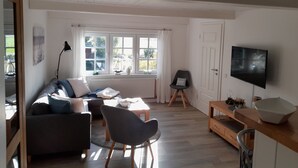 A modern living room with a sofa, chairs, a TV, and a dining area. - Liebevoll Saniertes Ferienhaus in Ruhiger Warftlage in Dagebüll-kirche (Dagebüll-Kirche)