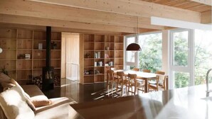 Een ruime woonkamer met een grote houten boekenkast, een eettafel met stoelen en een open haard.