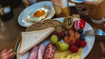 Un plato de desayuno con tostadas, jamón, queso, uvas, frutos rojos y una bebida.