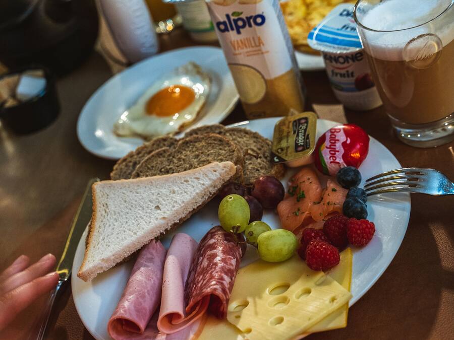 Un plato de desayuno con tostadas, jamón, queso, uvas, frutos rojos y una bebida.