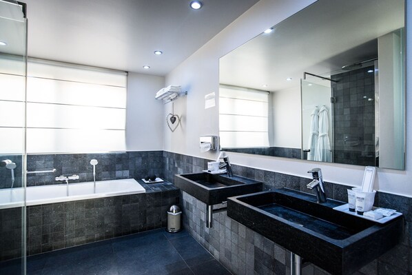 A modern bathroom with a large mirror, two sinks, a bathtub, and a shower.