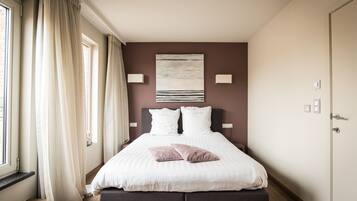 A neatly arranged bedroom with a bed, curtains, a wall-mounted artwork, and a door.