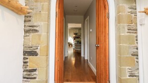 A stone archway leading to a hallway with wooden doors and a view into a kitchen area. - Upper Vestry (Llandysul)