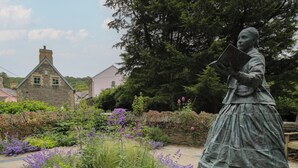 A statue in a garden with stone buildings in the background. - Upper Vestry (Llandysul)