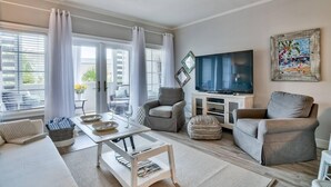 Uma sala de estar moderna com sofá, poltronas, televisão e área de jantar com mesa e cadeiras.