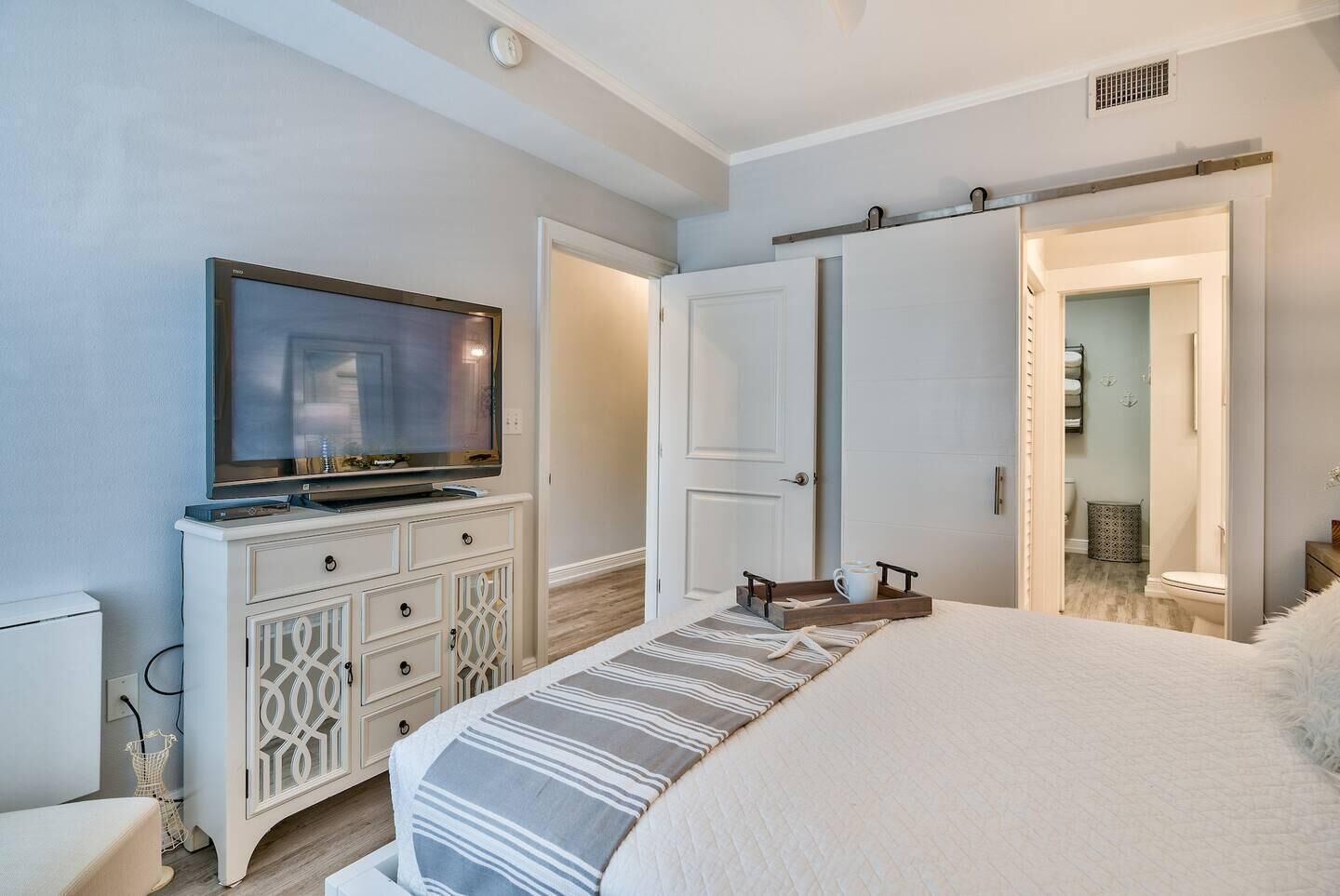 Une chambre à coucher avec un lit, un téléviseur posé sur une commode, une porte et une salle de bain visible à travers une porte ouverte.