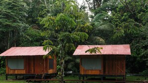 Two wooden cabins with corrugated metal roofs, surrounded by dense tropical foliage.