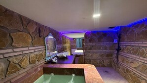 A stone-walled bathroom with a marble bathtub, a mirror, and a towel rack. - El Aljibe Relax (Córdoba)