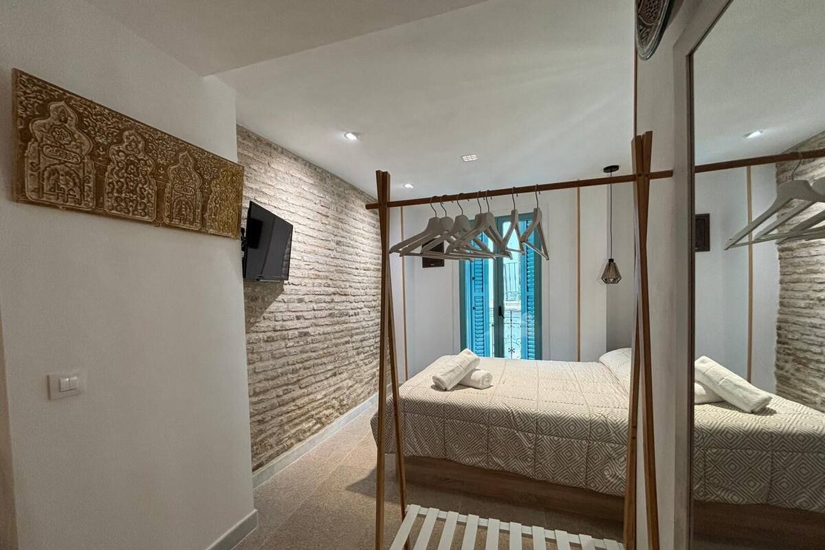 A bedroom with a bed, a wardrobe, a television, and a stone wall.