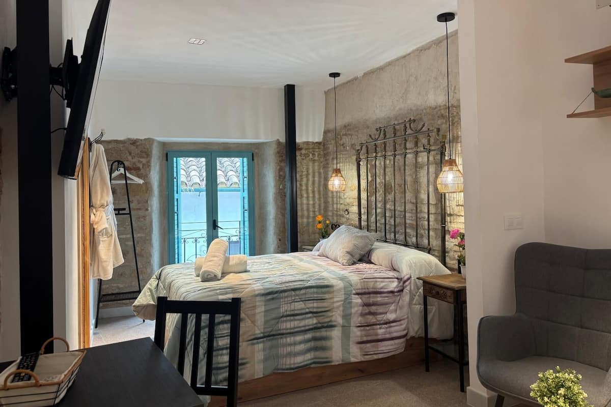 A bedroom with a bed, bedside table, chair, and a view of the outside.