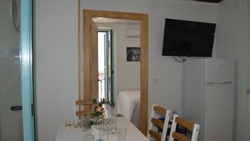 A dining area with a table set for four, a television mounted on the wall, and a refrigerator to the right.