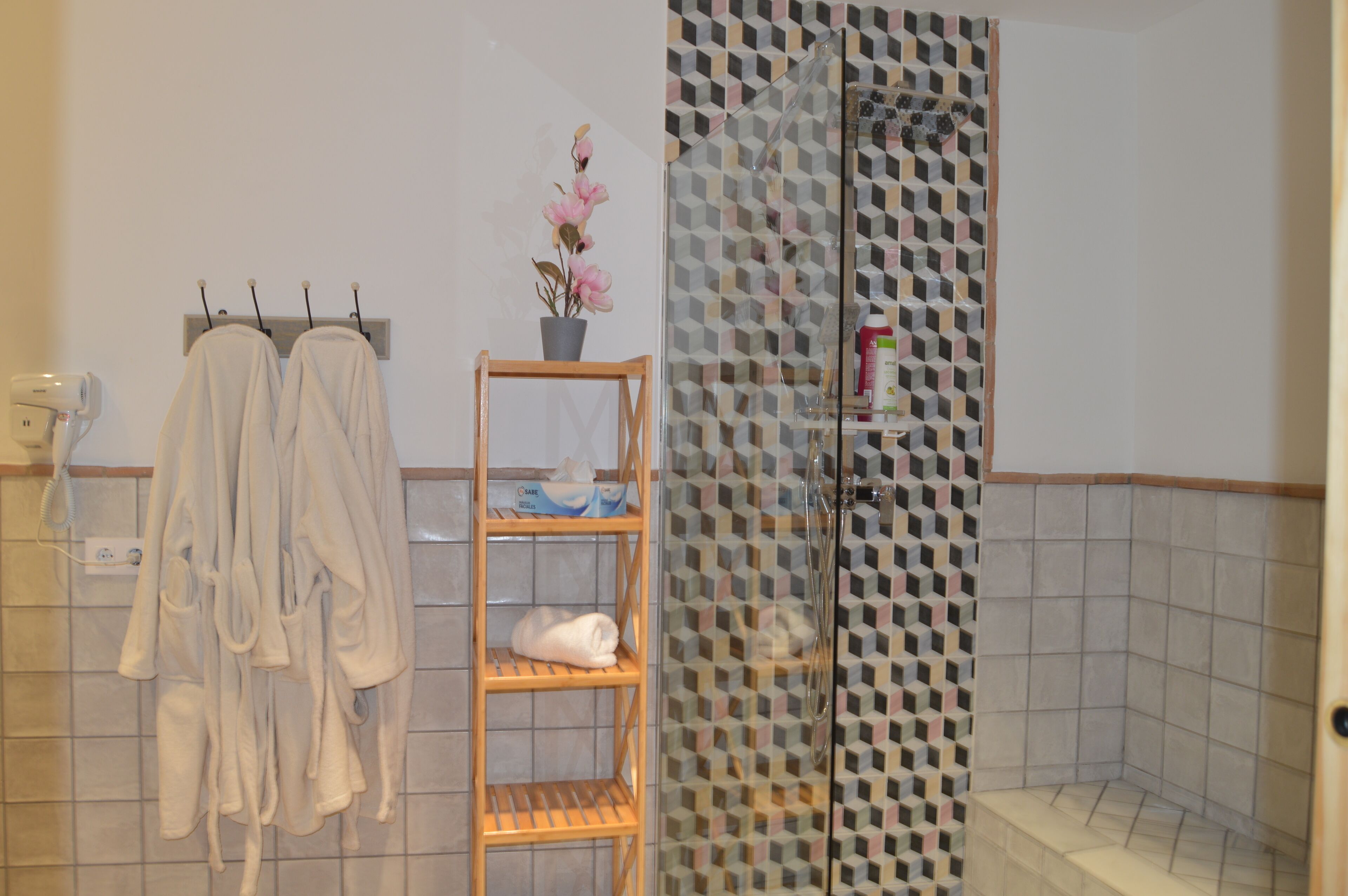A bathroom with a shower, a towel rack with towels, a shelf with toiletries, and a potted plant.