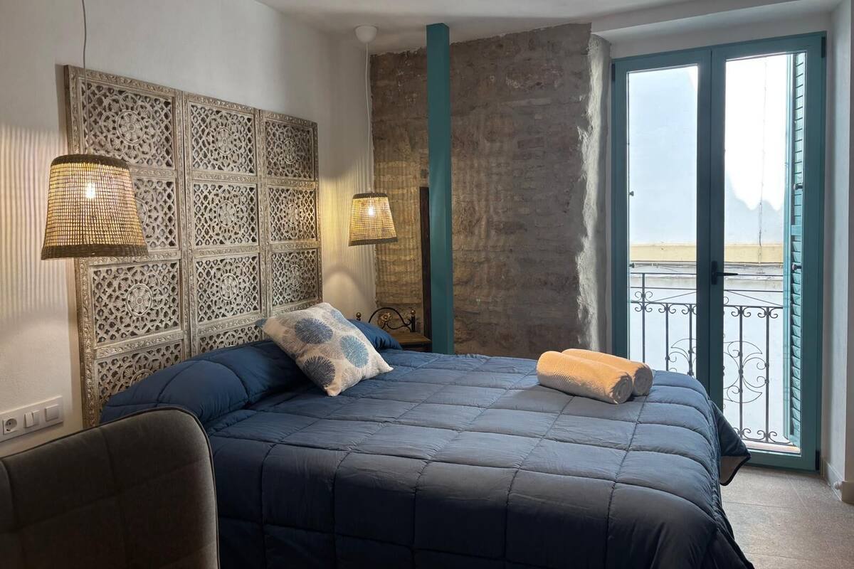A bedroom with a bed, decorative wall panels, a balcony with a view, and a door.