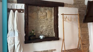 A rustic room with a stone wall, a wooden shelf with decorative items, a wooden drying rack, and a television mounted on the wall. - El Aljibe Relax (Córdoba)