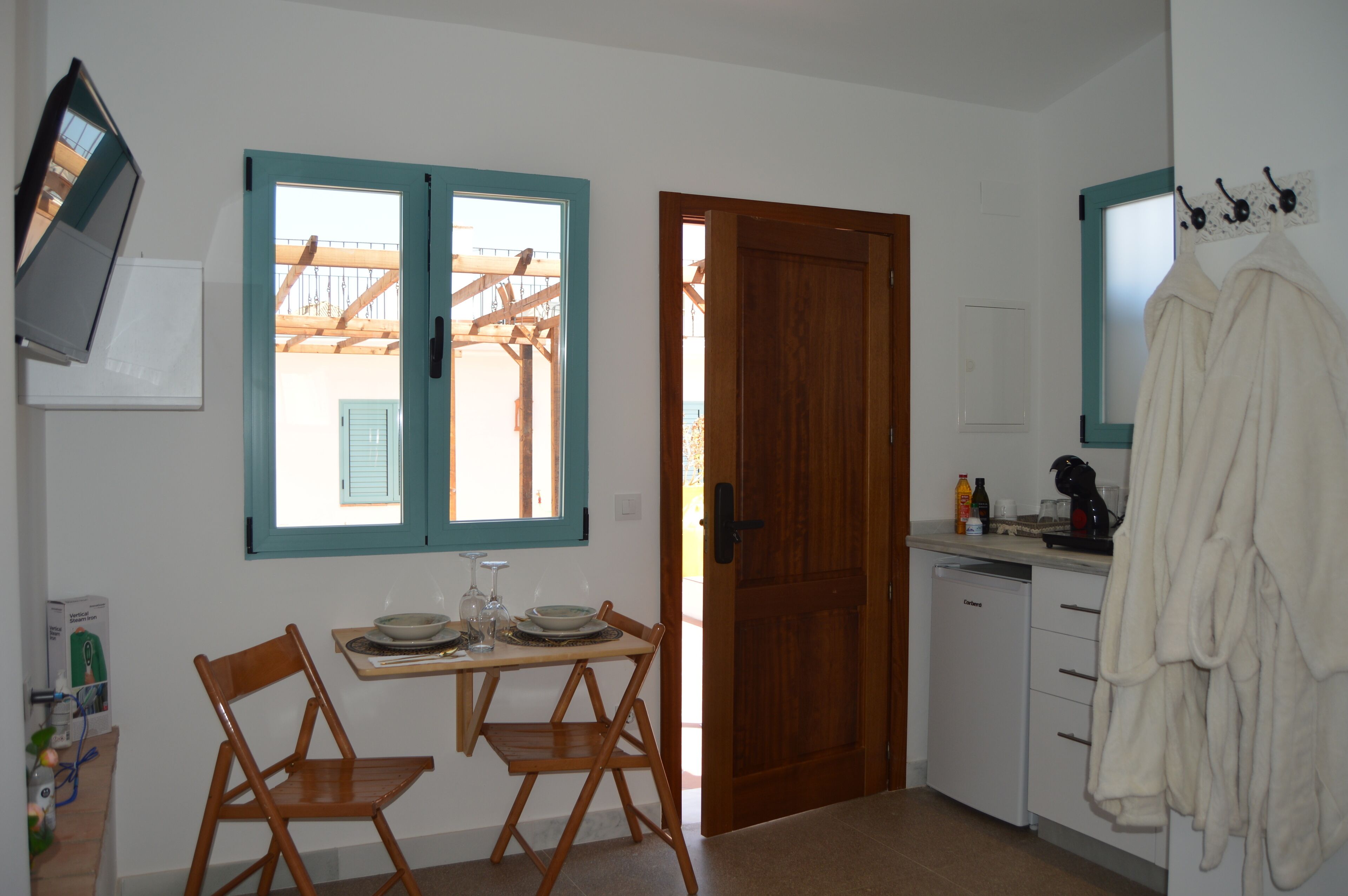 A compact kitchen with a dining area, a wooden door, and a window with a view of a balcony.