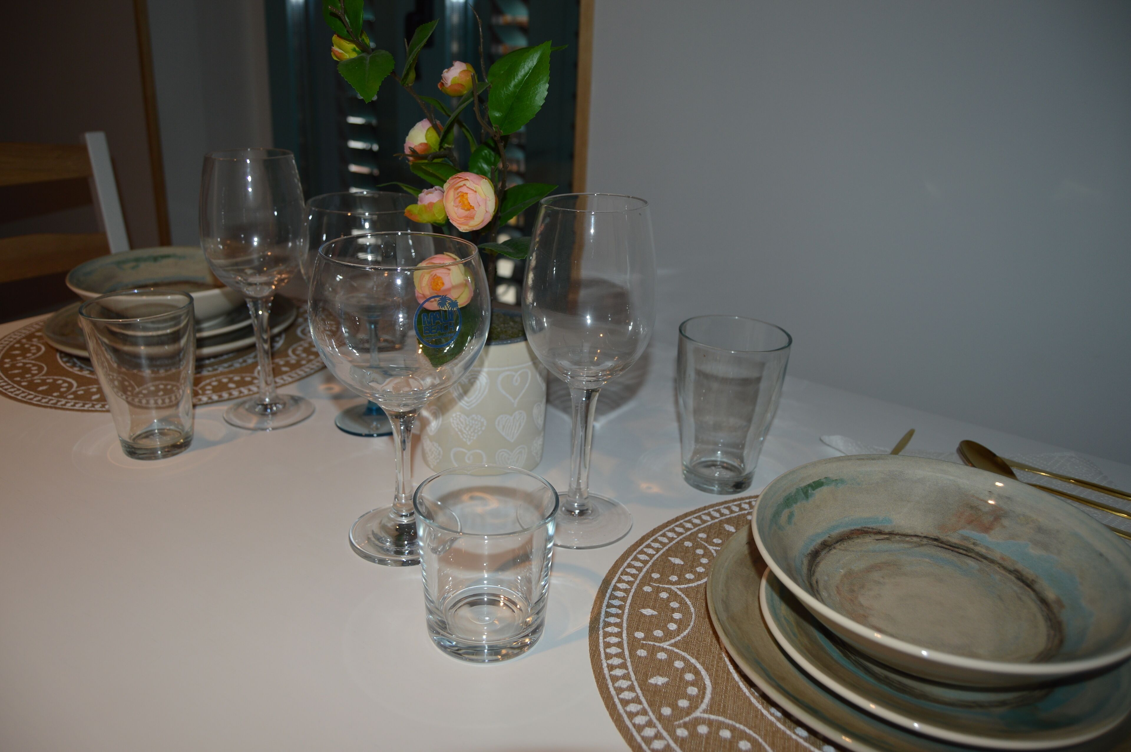 Ein Esstisch gedeckt mit Tellern, Gläsern und einer Blumenvase.