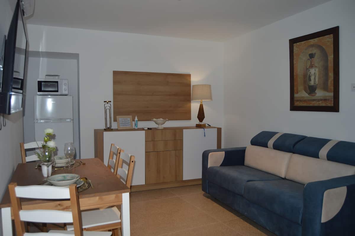 A compact living space with a dining area, a sofa, a microwave, a lamp, and a painting on the wall.