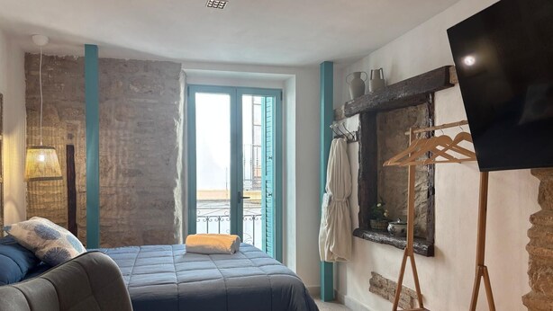 A bedroom with a bed, a chair, a TV, a balcony, and a stone wall. - El Aljibe Relax (Córdoba)