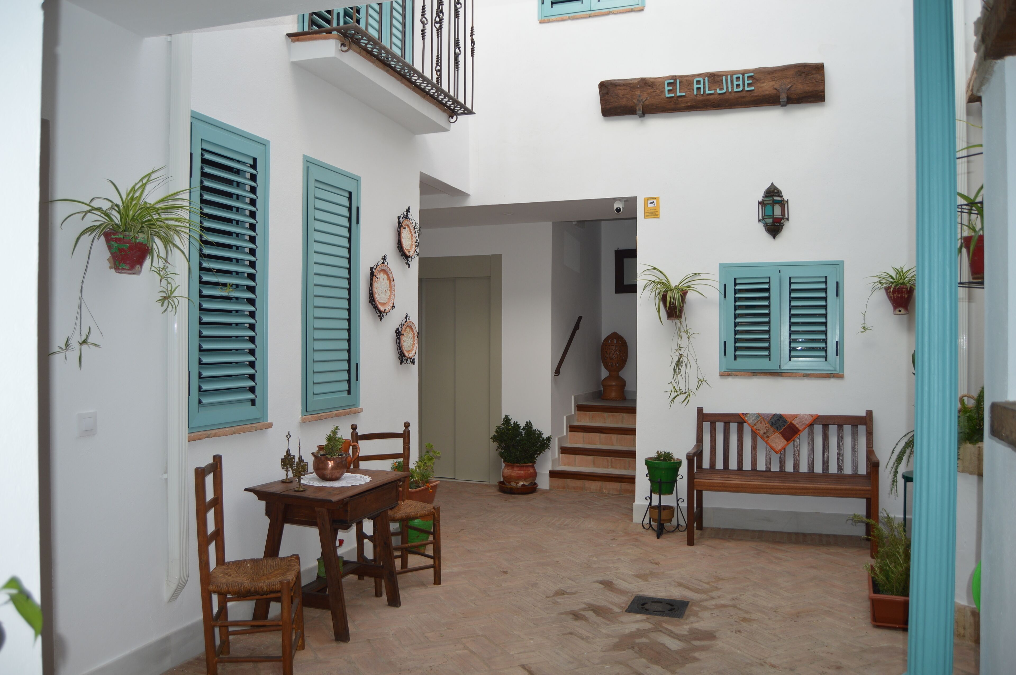 Un patio con un banco de madera, una mesa con sillas, plantas en macetas y una escalera que lleva a un nivel superior.