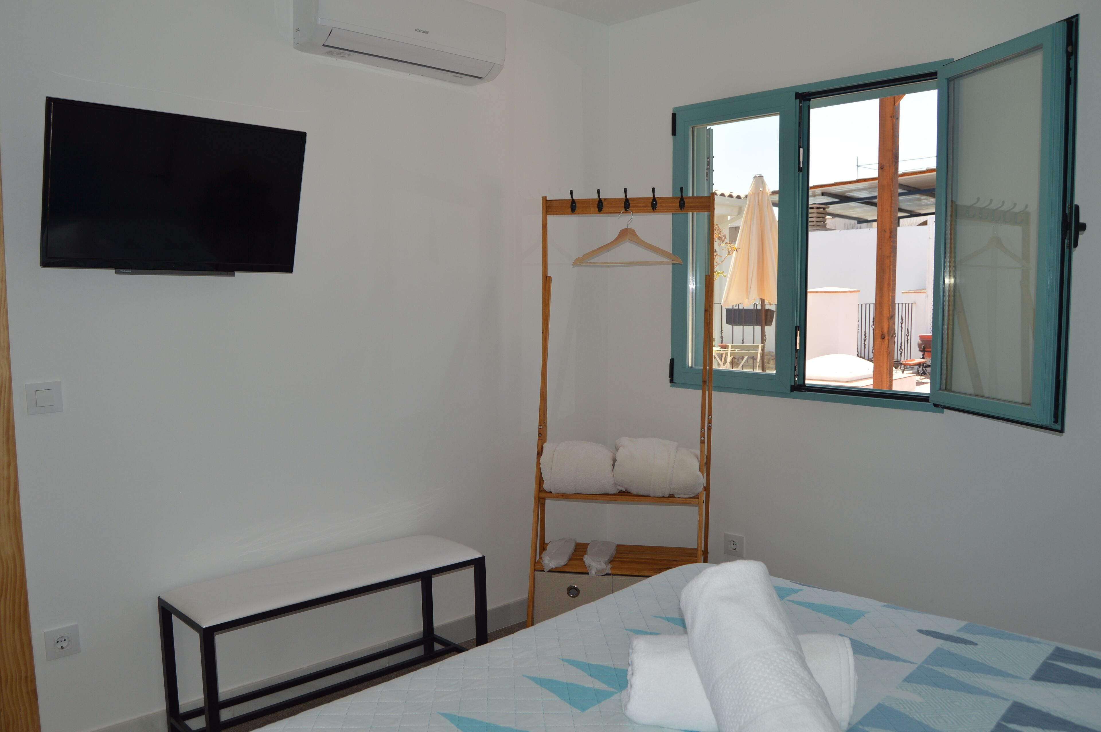 Un dormitorio con cama, una banca, televisor, armario y ventana con vistas.