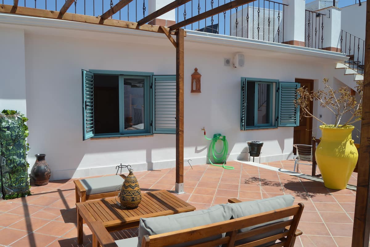 A terrace with wooden furniture, a yellow vase, and a green hose.