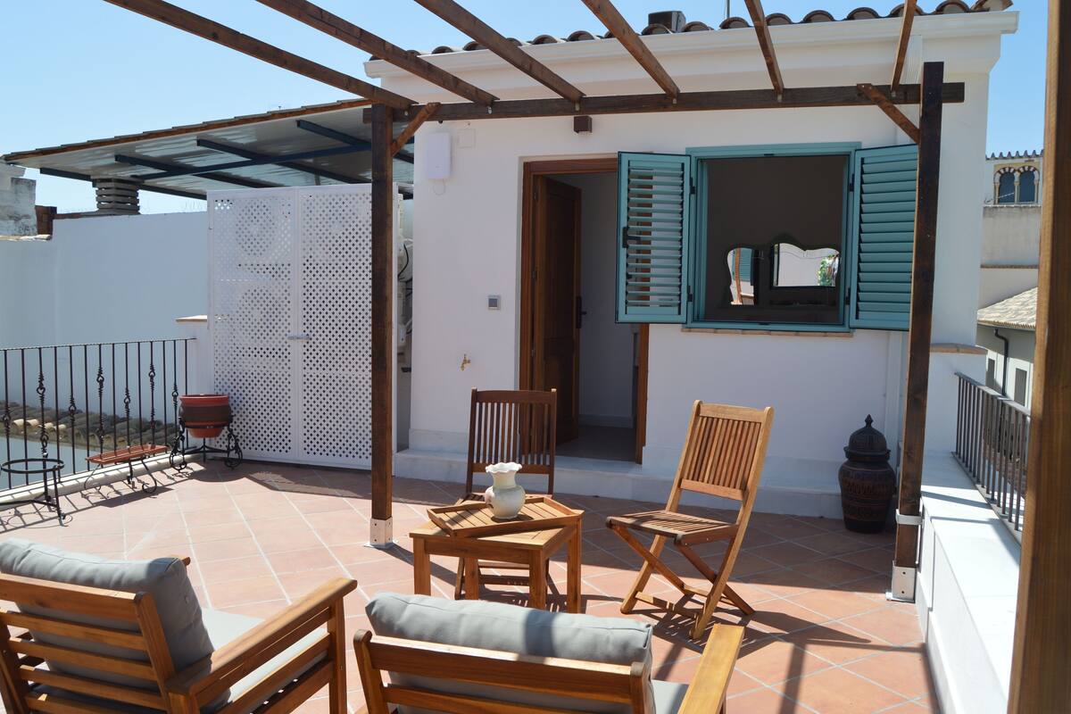 A covered outdoor seating area with wooden furniture and a tiled floor.