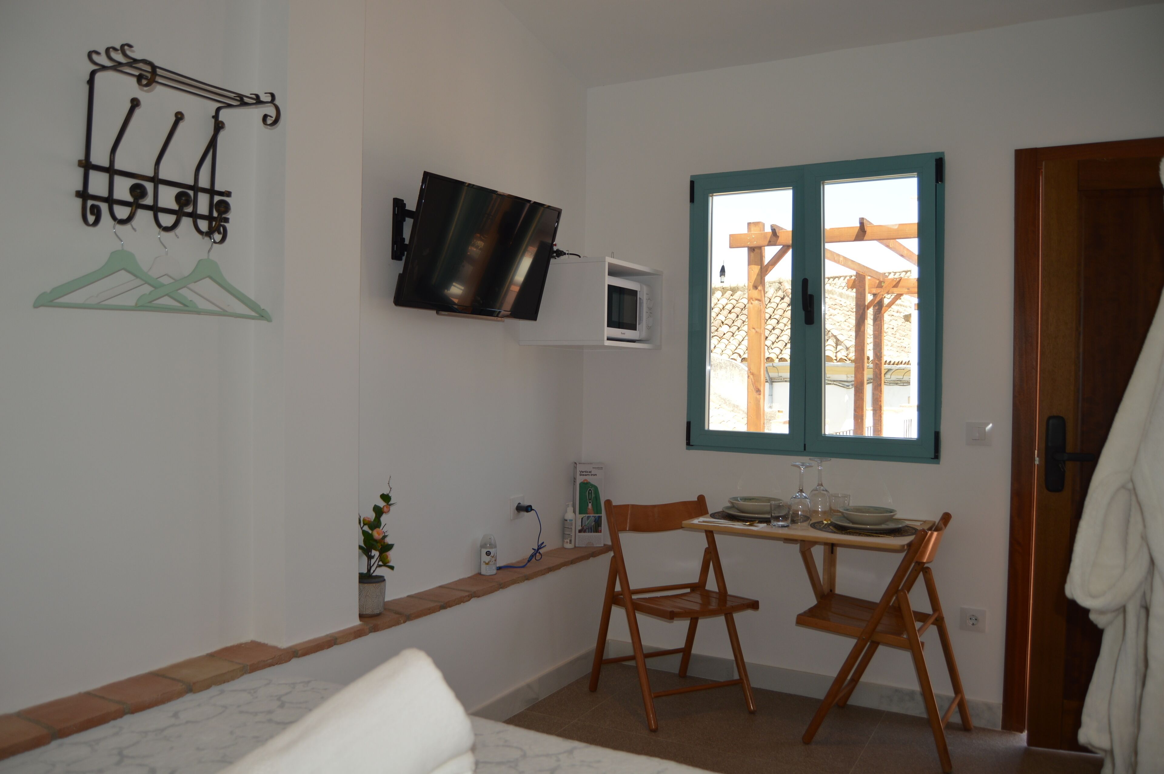 Una stanza piccola con un letto, un tavolo con sedie, una TV a parete, una finestra con vista e una porta.
