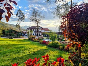 Ein großes, zweistöckiges Gebäude mit Garten, umgeben von Bergen.