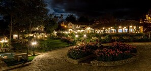 Ein gut beleuchtetes Hotel mit mehreren Gebäuden, einem Blumengarten und einem Poolbereich.