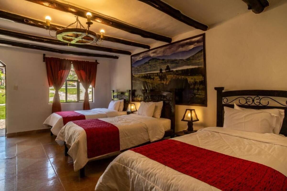 A hotel room with two beds, red and white bedding, a chandelier, a painting of a landscape, and a window with red curtains.