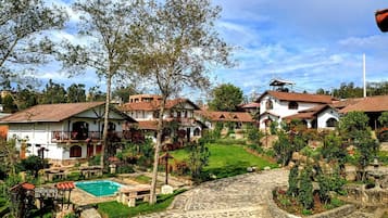Un village traditionnel avec des chemins pavés de pierres, une piscine centrale et des bâtiments blancs aux toits recouverts de tuiles rouges.
