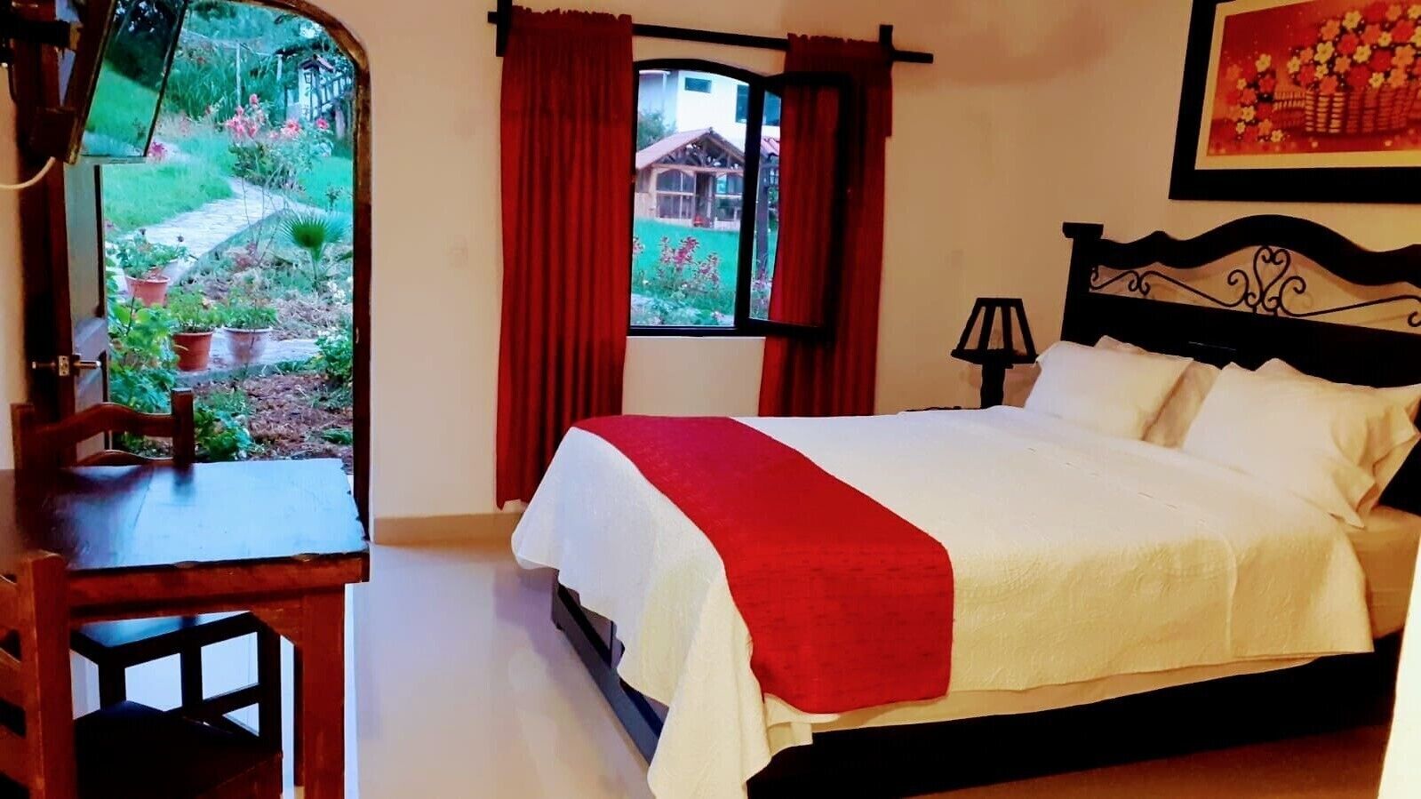 A bedroom with a bed, a desk, and a window with curtains.