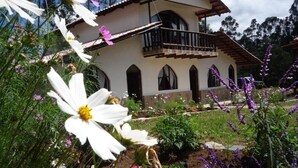 A two-story house with a balcony, surrounded by a garden with various flowers and plants. - Hotel Villa de Paris (Chachapoyas)