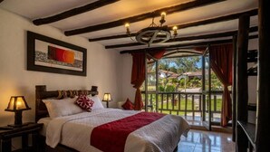 A bedroom with a bed, two bedside tables, a chandelier, a window with curtains, and a view of the outdoors. - Hotel Villa de Paris (Chachapoyas)