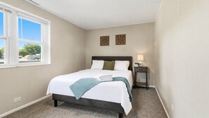 A hotel room with a bed, a nightstand, a window, and a wall-mounted artwork.