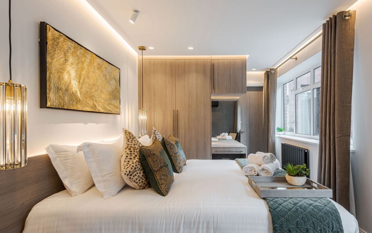 A modern bedroom with a large bed, a bedside table with a plant, a view of the bathroom, and a large abstract painting on the wall.