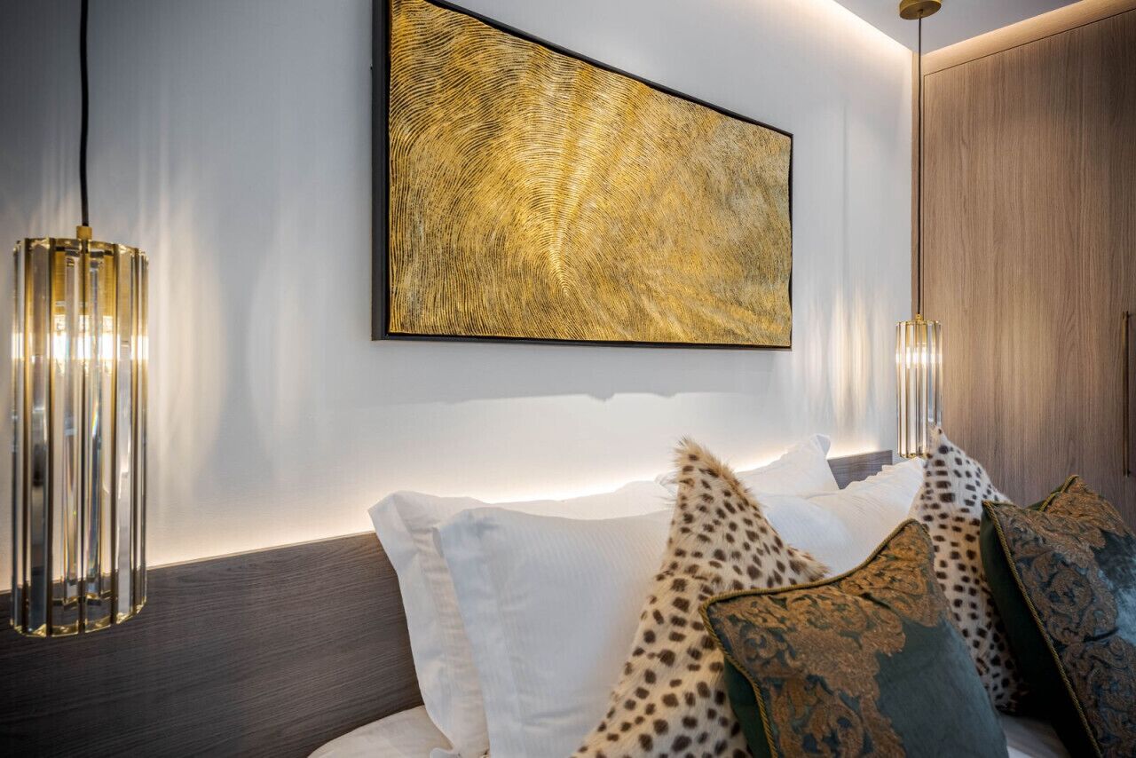 Un dormitorio moderno con una cama grande, dos lámparas fijadas a la pared y un cuadro abstracto de grandes dimensiones.