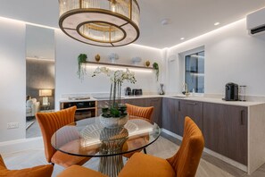 Een moderne keuken met een glazen eettafel, oranje stoelen en een kroonluchter.