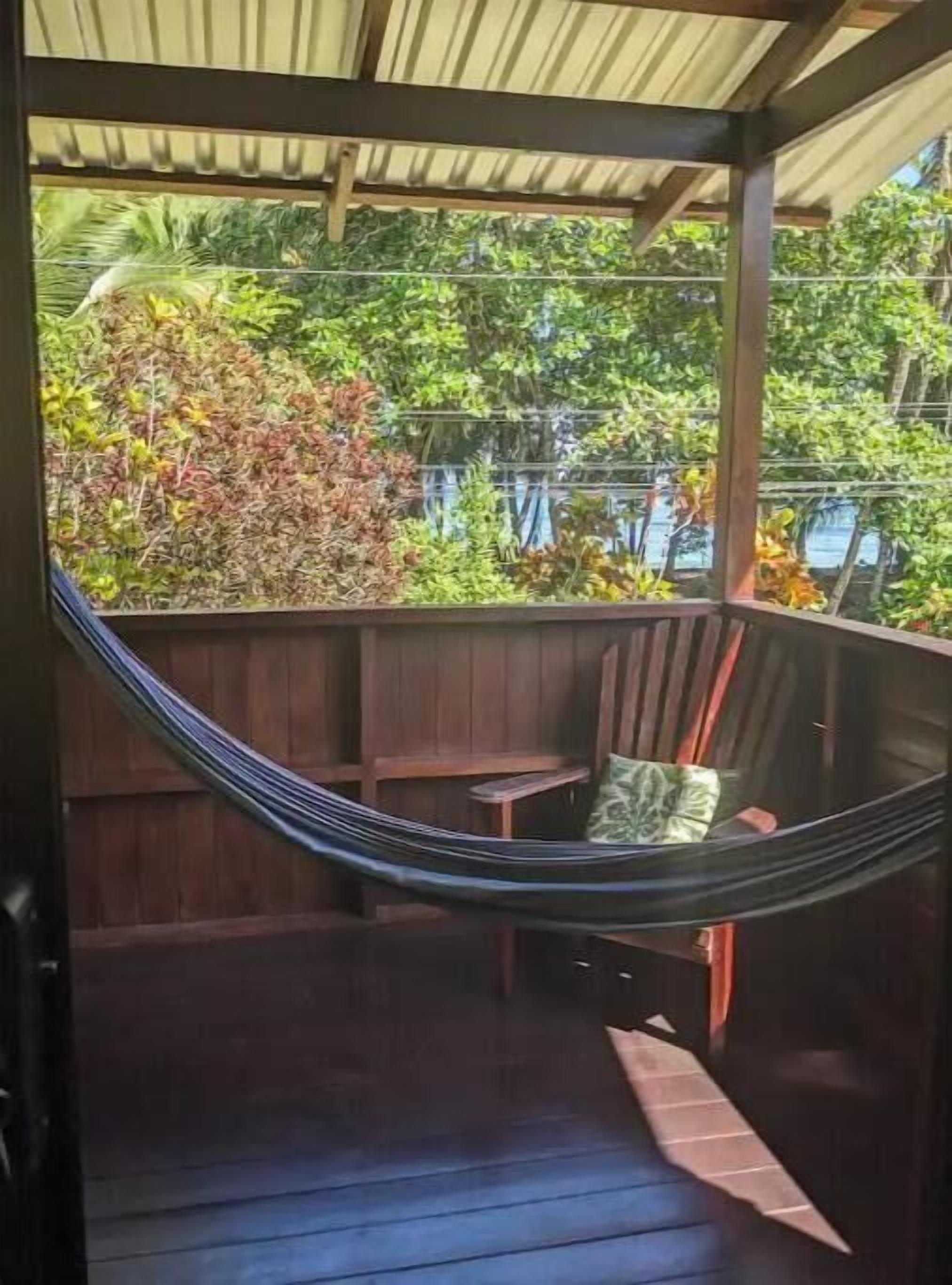 A hammock chair under a wooden pergola with a view of lush greenery and a body of water.