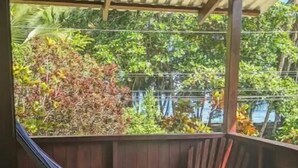 Een hangstoel onder een houten pergola met uitzicht op weelderige begroeiing en een wateroppervlak.