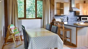 Een eethoek met een tafel voor vier personen, een kinderstoel en een keuken met moderne apparatuur.