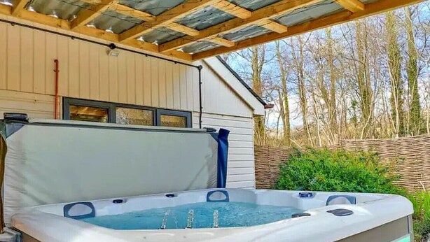 Een hottub met een deksel, een houten pergola erboven en een huis op de achtergrond.