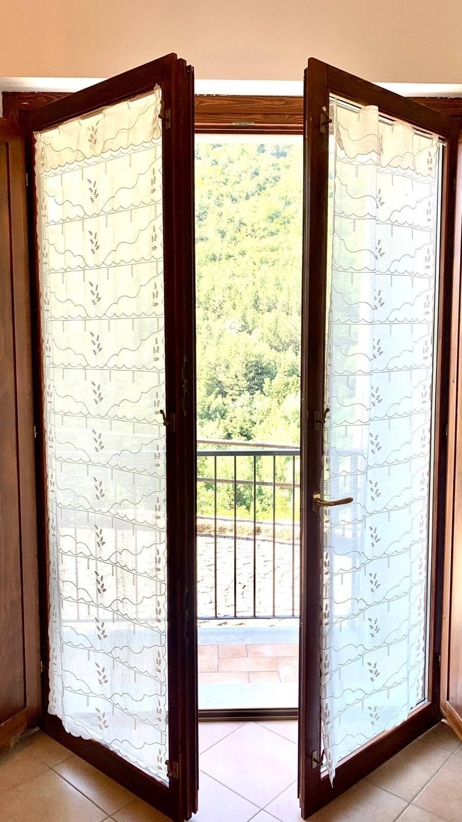 A set of glass doors with a metal gate in the center, leading to an outdoor area with a view of a green landscape.