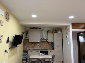 A compact kitchen with a dining table, cabinets, and a TV mounted on the wall. - Grazioso monolocale nel borgo dei cervi (Villetta Barrea)