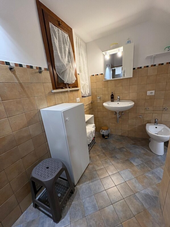 Une petite salle de bain avec un lavabo blanc, un bidet, un miroir et un petit tabouret.